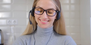 友好的呼叫中心话务员女士通过耳机通话。漂亮的白人女性，戴着眼镜，在笔记本电脑的网络摄像头上与客户交谈。帮助台专家在封锁期间在家工作