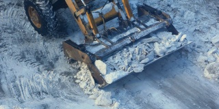 冬天的一天，一辆带着铲运机的拖拉机正在清理道路上的冰雪。道路机械正在清理积雪。市政交通、除雪机