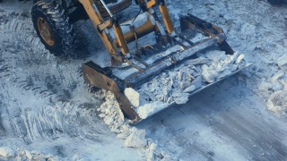 冬天的一天，一辆带着铲运机的拖拉机正在清理道路上的冰雪。道路机械正在清理积雪。市政交通、除雪机视频素材模板下载