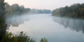 水上有烟。清晨拂晓时，雾漂浮在河上。绿色森林衬托下的美丽湖泊。大自然迷人的奇迹。水表面。文本的复制空间