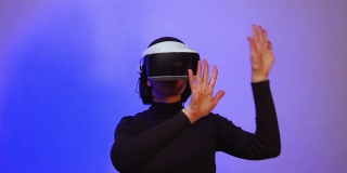 一个戴着虚拟现实头盔的女孩展开双臂，仿佛在推动着紫色霓虹灯的空间，全高清。虚拟世界的概念。虚拟空间的生活方式