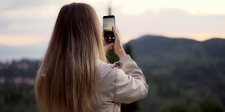 一名金发女子手持智能手机拍摄山景