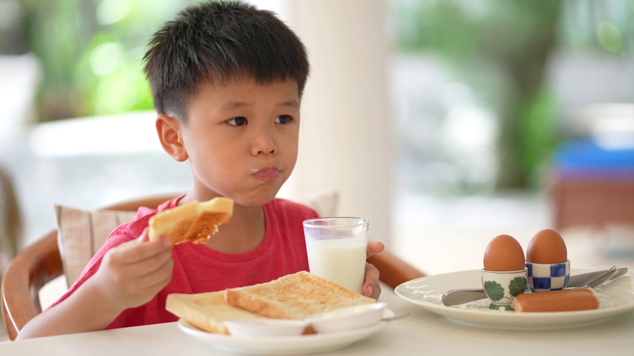 亚洲小孩早餐喝一杯牛奶。健康早餐的概念