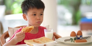 亚洲小孩早餐喝一杯牛奶。健康早餐的概念