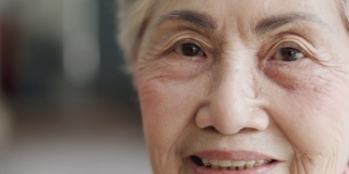 4K近景拍摄，一名80多岁的亚洲老年女性(80多岁)，头发花白，脸上带着快乐的表情和美丽的眼睛，对着镜头微笑，享受着退休生活。