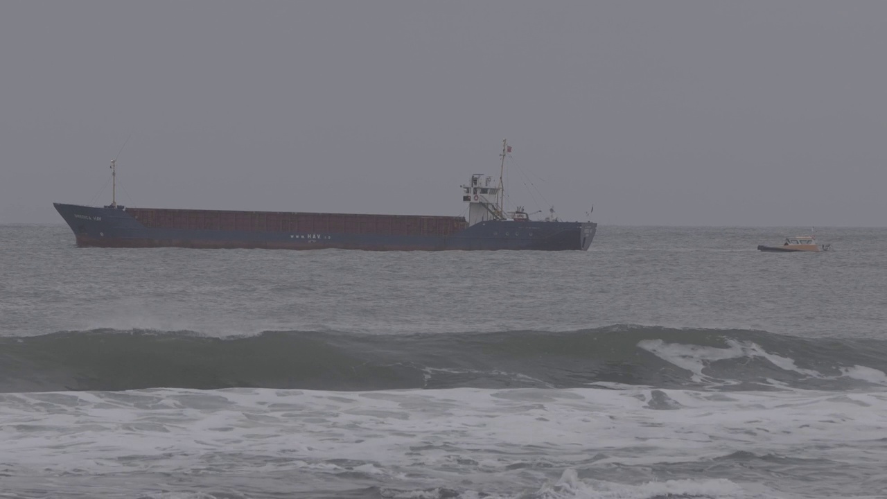 在暴风雨天气下，一艘油轮沿着一艘引航船在波涛汹涌的海面上行驶的特写镜头