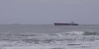 在暴风雨天气下波涛汹涌的海面上，一艘油轮沿着一艘领航船和一艘军用船的镜头在背景中出现