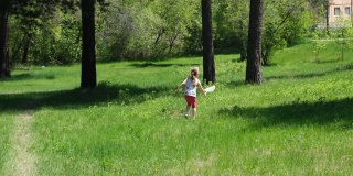 在阳光明媚的夏日里，可爱的小女孩一边走一边用勺子网捉蝴蝶