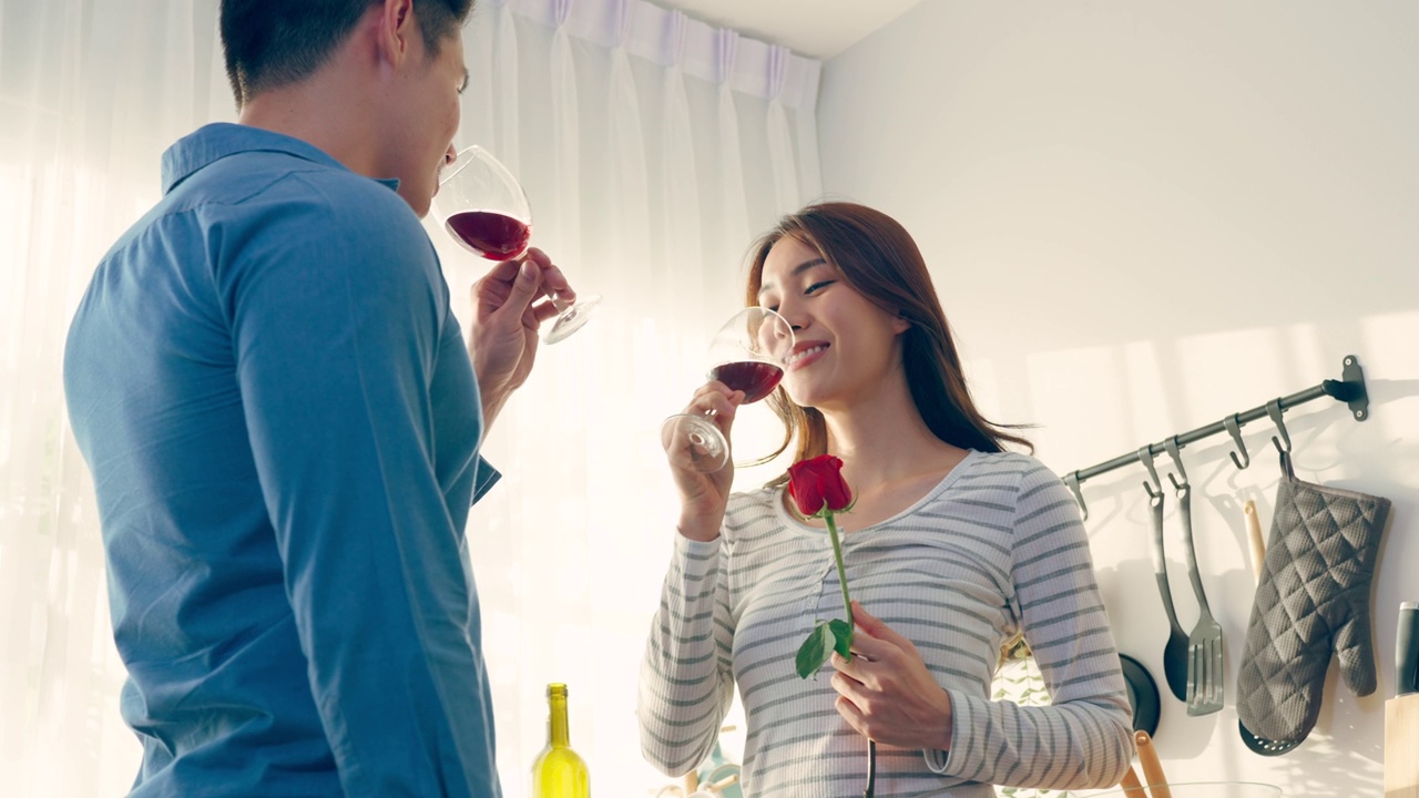 亚洲年轻情侣在情人节举杯畅饮。可爱浪漫的新婚男女在家里厨房共进晚餐庆祝结婚纪念日