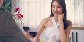 亚洲年轻情侣共进晚餐庆祝情人节。迷人浪漫的新婚男女在家里的厨房里举行晚会，在餐桌上吃结婚纪念日的食物。