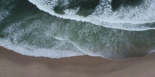白色的小波浪拍打着暗绿色海水的沙滩。