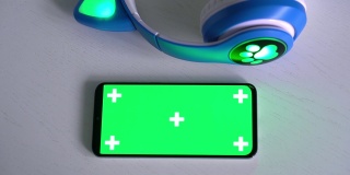 智能手机空白绿色屏幕模型与儿童无线耳机隔离在灰色背景