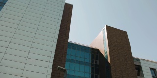 一座相当高的商业建筑，玻璃倒映着天空。在拍摄对象时，相机平稳地倾斜