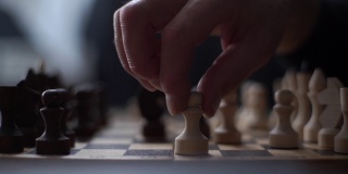 在黑暗的房间里，无法辨认的国际象棋选手表演与棋子在木制棋盘上移动的特写侧面视图。