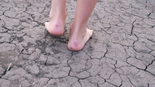 光着脚的女孩走在干涸的湖面上，干旱，土地裂缝，没有水。视频素材模板下载