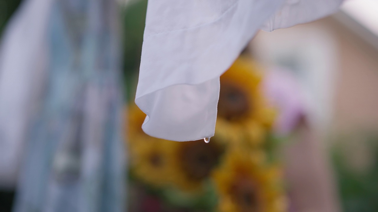 特写镜头:从洗净的白布上缓缓落下的湿滴。新鲜的衣服在户外晾晒在春天夏天的后院