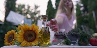 女性手拿着盛有葵花籽油的玻璃玻璃瓶在户外慢动作烹饪沙拉。模糊年轻苗条的白人妇女准备健康的午餐在后院