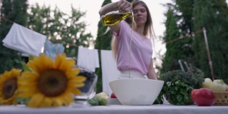 在夏日春日的户外，食用油在白色的碗里以慢镜头倒入。模糊的年轻白人女子在后院用植物油做沙拉。烹饪和生活方式