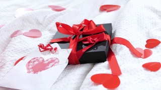 礼盒包装好，明信片上装饰着一个美丽的红色蝴蝶结放在床上。情人节礼物。视频素材模板下载