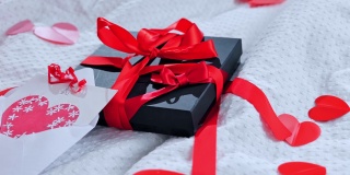 礼盒包装好，明信片上装饰着一个美丽的红色蝴蝶结放在床上。情人节礼物。