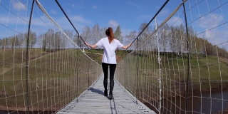 一名女子走在国家公园里一条小河上的索桥上。后视图