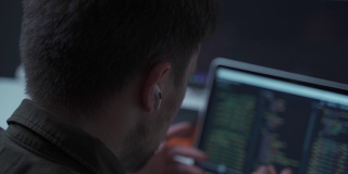 一名男性程序员在电脑前工作，使用入耳式耳机与同事或客户交谈。一名IT开发人员在工作时，耳朵里插着一个白色的无线小耳机