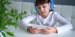 在客厅的沙发上，孩子戴着蓝色耳机，用白色智能手机听音乐