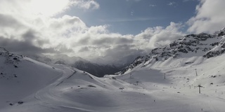 在冬天，蜿蜒的小路穿过被雪覆盖的山峰，阳光透过云层在蓝天中窥视