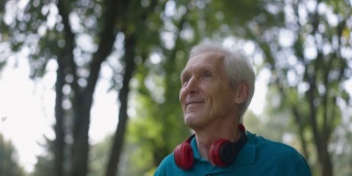 特写快乐的老年人健康的人慢跑在阳光户外微笑看着别处。自信的白人退休人员在夏季春天公园慢动作锻炼跑步的肖像。运动和健康。