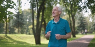快乐的老人在户外的阳光下慢跑，环顾四周微笑。健康的白人退休运动员的肖像在夏季春天公园欣赏自然的慢动作跑步。生活方式和运动。