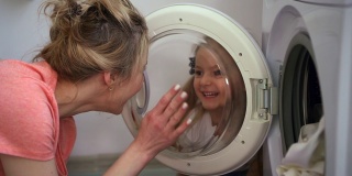 女人和小女孩把脏衣服装进洗衣机里。在洗衣机里装满衣服。女儿