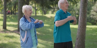中等身材的老年夫妇在阳光明媚的户外公园同时热身锻炼。自信快乐的白种人夫妻训练慢动作。生活方式和运动理念。