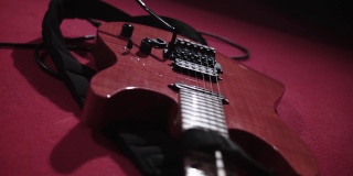 红色地板上放着一把红色电吉他的特写镜头。音乐会上用电吉他演奏的流行音乐。这把吉他调好音，准备参加摇滚乐队的演出。乐器焦距不清