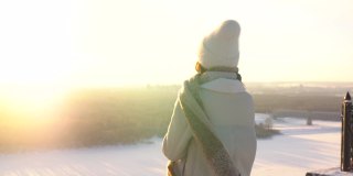 跟踪拍摄的快乐的年轻女子，在美丽的冬季雪景上欣赏观景台，喝着热咖啡。