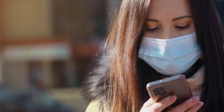 一名妇女戴着防空气污染和冠状病毒的医用口罩，在城市街道上用手机打字