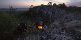 手持火炬手，夜山游。一对年轻的游客在夜间攀爬一座高山，手上拿着手铐和火炬