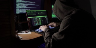 一名黑客在暗室里的显示器前试图黑进安全系统