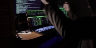 一名黑客坐在暗室里的显示器前，对着安全系统的入侵感到高兴