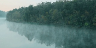 水上有烟。清晨拂晓时，雾漂浮在河上。绿色森林衬托下的美丽湖泊。水表面。大自然迷人的奇迹。文本的复制空间