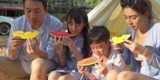 幸福的亚洲家庭在节日帐篷前吃西瓜