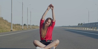 一位年轻女子坐在柏油路上，高兴地举起双手。