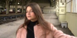 火车站月台上，一个穿粉红色外套的年轻妇女面带微笑地站着。等待