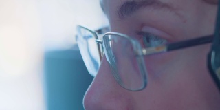 一个戴眼镜的少年的眼睛特写——他的眼睛在电脑显示器上转动