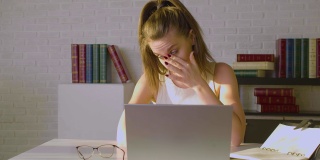 一位疲惫的年轻女子坐在一台笔记本电脑前，她摘下眼镜，按摩着鼻梁。最后期限的概念
