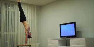 一个肌肉发达的男人一边做倒立一边看电视。理念独到，创意出众