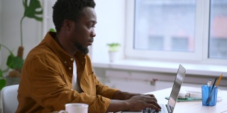 非洲人在家庭办公室用笔记本电脑打字。记者写一篇文章。20多岁的美国人