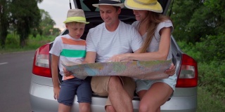 一家人坐在汽车后备箱里学习地图。坐汽车长途旅行。家庭