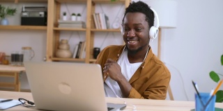 一名非洲男子戴着耳机听音乐，在家里的桌子旁通过Spbas电脑跳舞