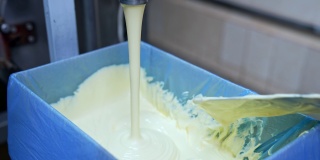 生产黄油的工厂。乳白色的乳制品倒入盒内。在奶场制作新鲜黄油。乳制品生产商。工人的手在搅拌黄油。特写镜头。