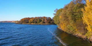 河边有五颜六色的树木。秋天的自然景观。秋天的风景很美。蓝色的湖在黄色的树的背景上。